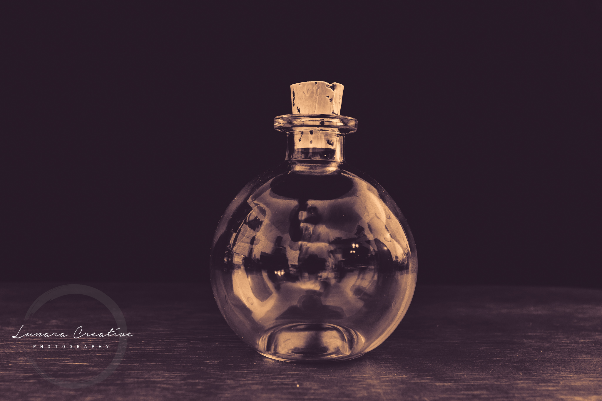 Tiny Bottle A tiny bottle sitting on a table.  Photo was tinted with a hint of purple color. by Lunara Creative Photography