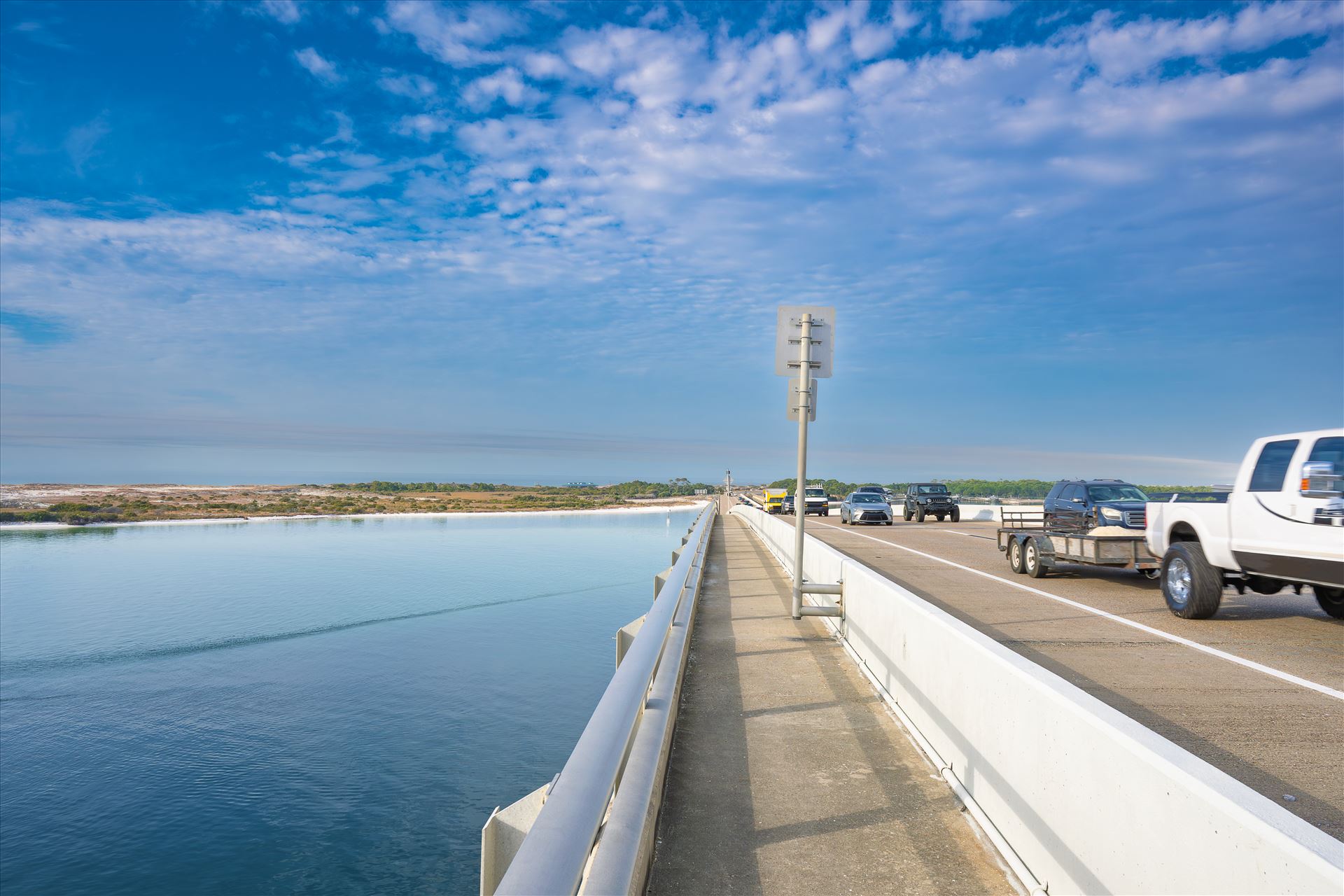 vehicle bridge with walking path at destin harbor vehicle bridge with walking path blue sky blue water no people cars and trucks at destin harbor by Terry Kelly Photography