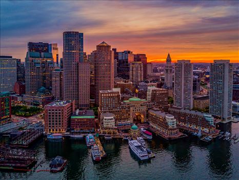 A beautiful sunset illuminates the sky behind the historic downtown Boston waterfront of Boston Harbor in Boston, Massachusetts by New England Photography