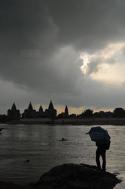 Monuments- Palaces and Temples of Orchha DSC_0337 Orchha, Madhya Pradesh, India- August 20, 2012: Chhatris on the bank of river Betwa, a tourist holding umbrella enjoying cloudy- rainy weather at Orchha, Madhya Pradesh, India. by Anil