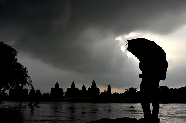Monuments- Palaces and Temples of Orchha Orchha, Madhya Pradesh, India- August 20, 2012: Chhatris on the bank of river Betwa, a tourist holding umbrella enjoying cloudy- rainy weather at Orchha, Madhya Pradesh, India. by Anil