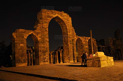 Monuments- Qutab Minar in Night, New Delhi, India. The Beauty of arches of  Iltutmish screen and some tourists standing near the  iron pillar in night at Qutub Minar Complex, Mehrauli , New Delhi, India. by Anil