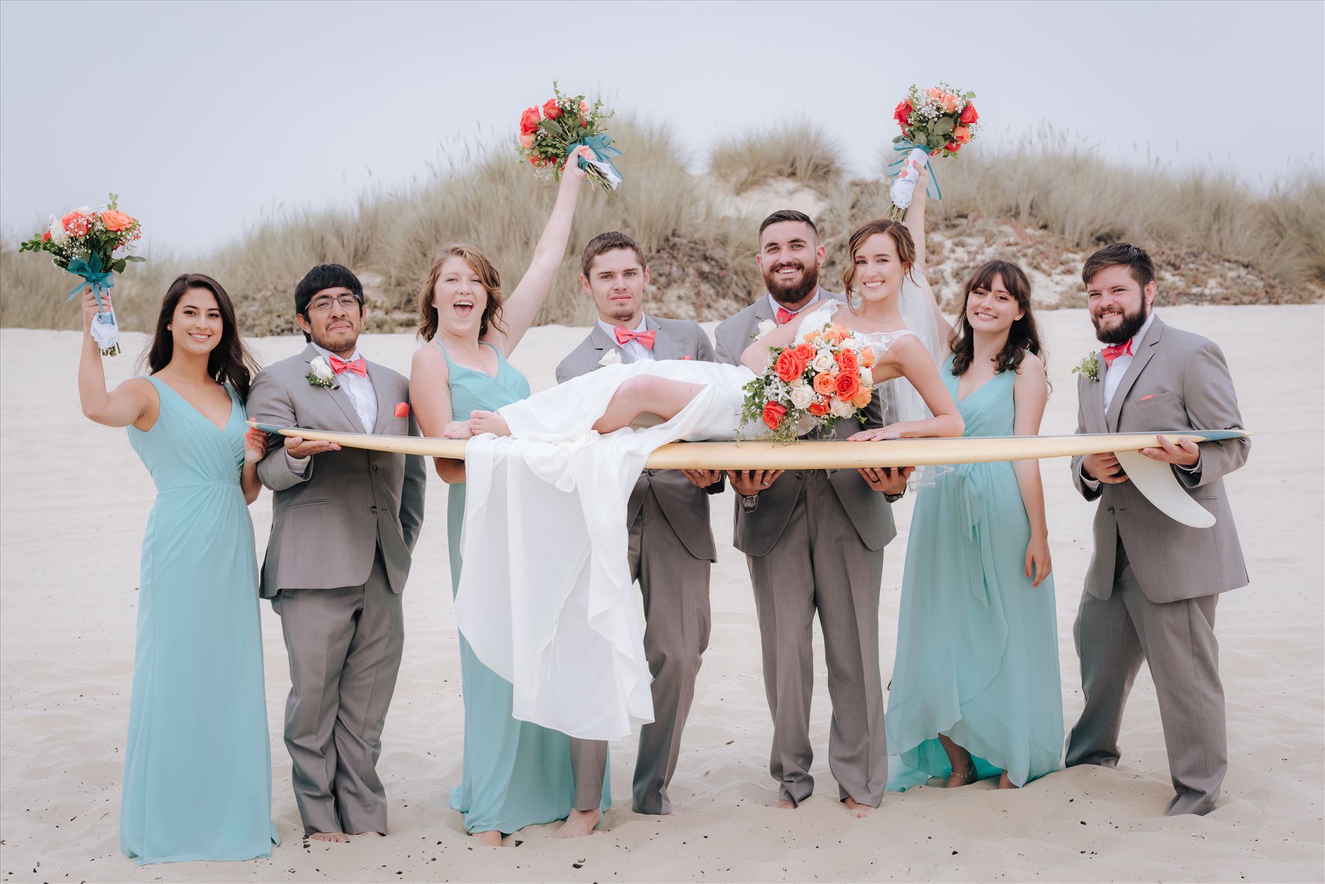 Sydney and Matthew 096 Mirror's Edge Photography a San Luis Obispo Wedding Photographer captures Sydney and Matthew's Wedding on the Beach in Grover Beach, California. Bride, groom and bridal party having fun with surfboard on the beach in california wedding style by Sarah Williams